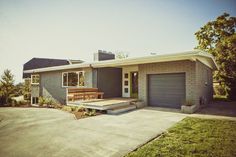 a gray house with a wooden deck in the front yard and two garages on each side