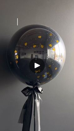 a black balloon with yellow dots on it and a ribbon tied around the bottom, hanging from a gray wall