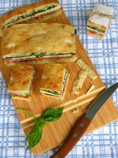 a cutting board topped with cut sandwiches next to a knife and some other food items