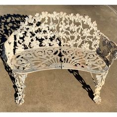 a white bench sitting on top of a cement floor next to a sidewalk with shadows