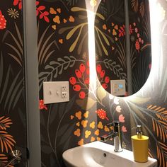 a sink and mirror in a room with floral wallpaper on the walls behind it