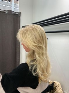 a woman with long blonde hair standing in front of a shower curtain looking at her reflection