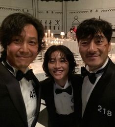 two men and a woman in tuxedos posing for a photo