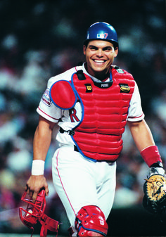 a baseball player with catchers gear on holding a glove and smiling at the camera