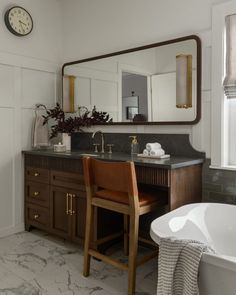 a white bath tub sitting next to a wooden counter top under a large framed mirror