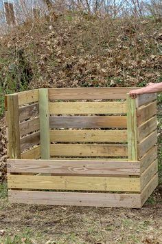 a person standing next to a wooden crate in the grass and bushes behind it, with one hand on top of the box