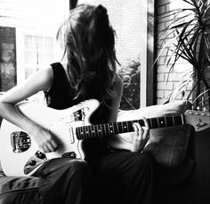 a woman sitting on a couch playing an electric guitar in front of a potted plant