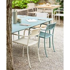 an outdoor table and chairs are set up in the gravel near a tree with two vases on it