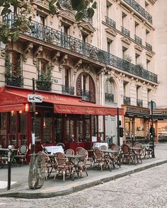 tables and chairs on the sidewalk in front of a building with red awnings