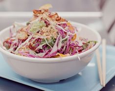 a white bowl filled with salad and chopsticks on top of a blue plate