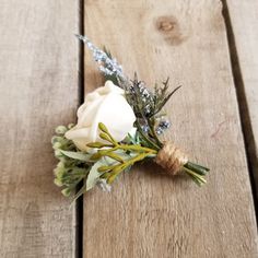 a boutonniere with white flowers and greenery on a wooden table top