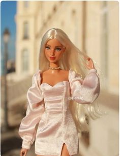 a barbie doll with blonde hair wearing a white dress and gold choker, standing in front of a building