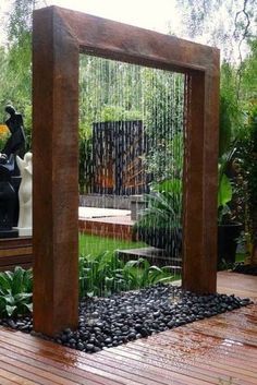 an outdoor fountain in the middle of a wooden deck with rocks and plants around it