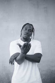 a man with dreadlocks standing in front of a gray wall holding his hands together