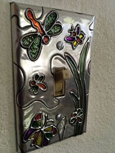 a decorative light switch cover with flowers and butterflies painted on the glass paneled wall