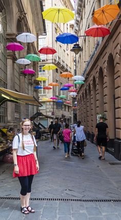 a woman standing in the middle of an alley with many umbrellas hanging above her