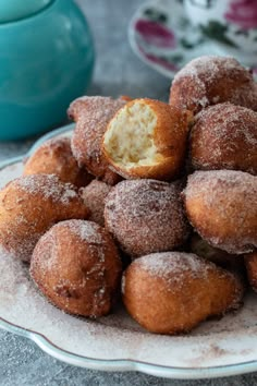 powdered sugar covered donuts on a plate with a tea pot in the background