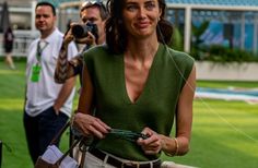 a woman holding a camera in front of some people on the grass and taking pictures