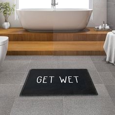 a bathroom with a bathtub, toilet and rug that says clothes off