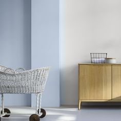 a white wicker baby carriage sitting in front of a blue wall and wooden cabinet