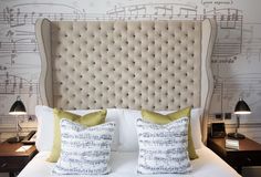 a white bed topped with two pillows and musical notes on the wall behind it's headboard