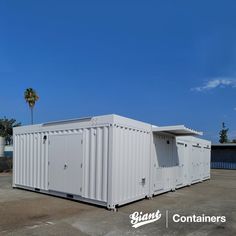 two white shipping containers sitting on top of a parking lot next to palm trees and blue sky