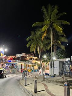 palm trees line the street at night in front of shops and stores on an island