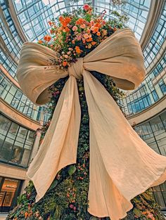 a very tall christmas tree with flowers on it's side in a large building