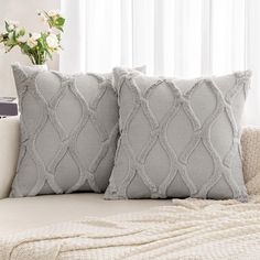 two gray pillows sitting on top of a white couch next to a vase with flowers