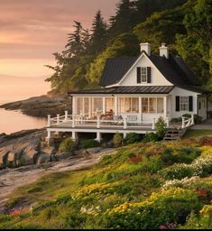 a white house sitting on top of a lush green hillside next to the ocean at sunset