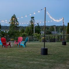 several lawn chairs and umbrellas are in the yard with string lights strung over them