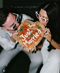 a man and woman holding up a heart shaped pizza with the words just married written on it