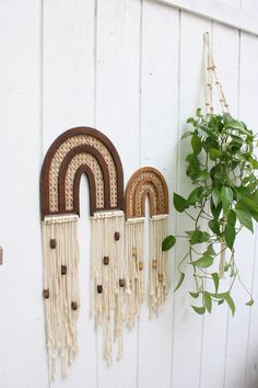 three decorative wall hangings on the side of a white building with a potted plant next to them