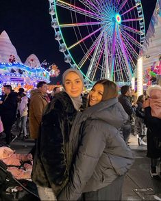 two women standing next to each other in front of a ferris wheel