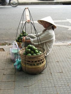 a woman sitting on the sidewalk with a basket full of fruit