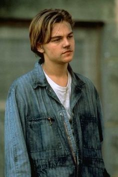 the young man is wearing a denim jacket and looking off into the distance with his hands in his pockets