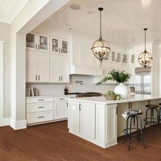 a large kitchen with white cabinets and wood flooring on the walls, along with two bar stools