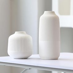 two white vases sitting on top of a table