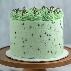 a cake with green frosting and chocolate sprinkles on a wooden stand