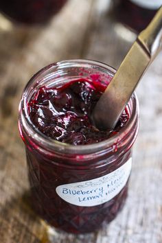 a jar filled with blueberry jam on top of a wooden table next to a knife