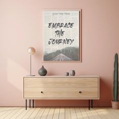 an empty room with pink walls and a wooden dresser in the foreground, there is a poster on the wall that says embrace the journey