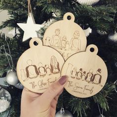 two wooden christmas ornaments with the names of three families on them, hanging from a christmas tree