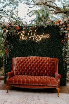 an orange velvet couch sitting in front of a lush green wall with the words, they hyggnos on it