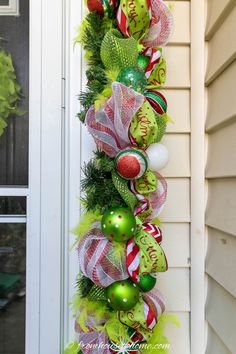 a christmas wreath hanging on the side of a house with green and red ornaments around it