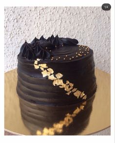 a black cake with gold decorations on top sitting on a table next to a wall