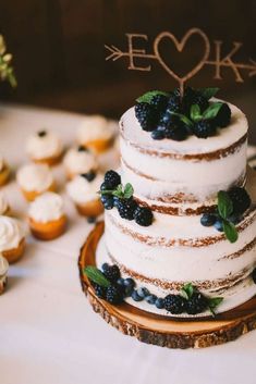 a wedding cake with blueberries and blackberries on top is surrounded by cupcakes