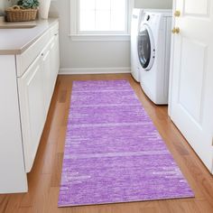 a washer and dryer in a room with wood floors, white cabinets and purple rug