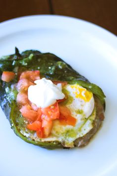 an egg in a green pepper on a white plate with sour cream and tomato slices