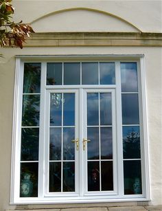 two white double doors with glass panes on the side of a building next to a tree