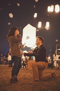 a man kneeling down next to a woman in front of a sky filled with balloons